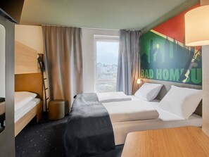 A hotel room with two beds, a desk, a chair, a window with curtains, and a wall with a cityscape poster. - B&B Hotel Bad Homburg (Bad Homburg v.d. Hoehe)