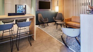 A modern hotel lobby with a bar area, seating, a flat-screen TV, and a vending machine.