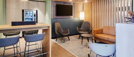 A modern hotel lobby with a bar area, seating, a flat-screen TV, and a vending machine.