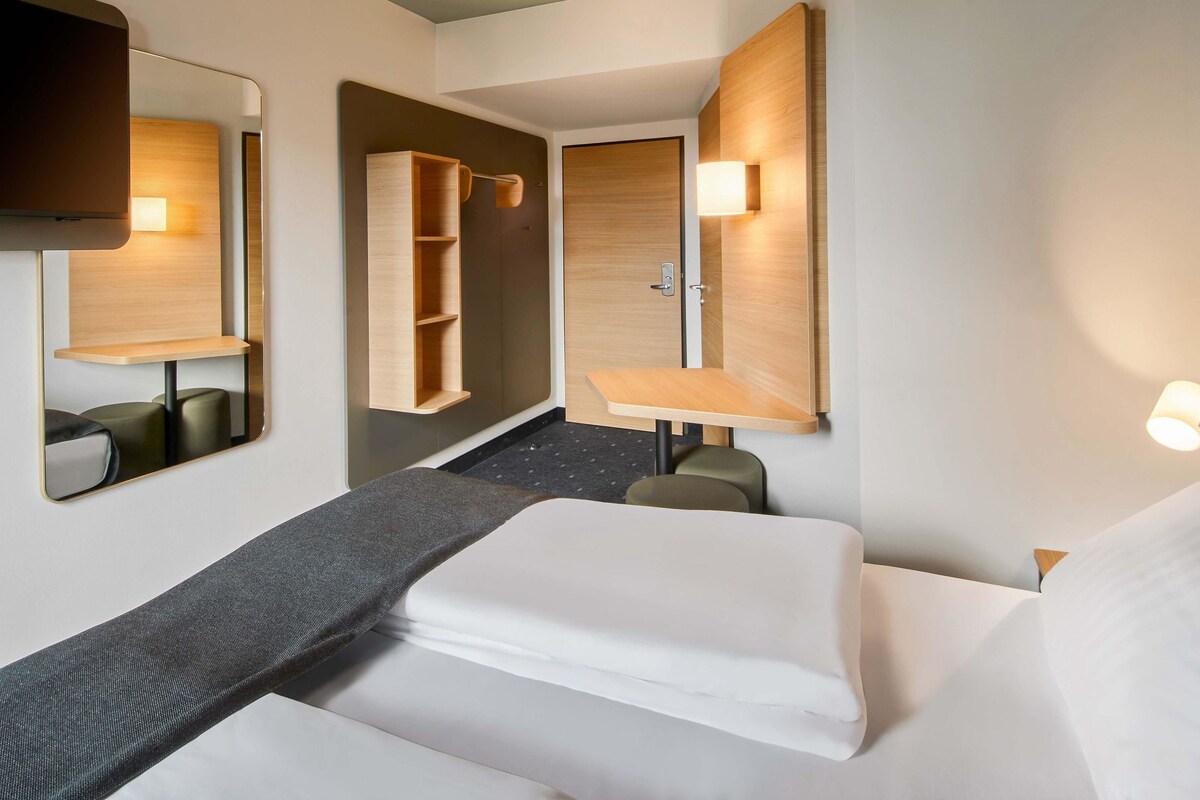Ein Hotelzimmer mit Bett, Schreibtisch, Spiegel und Kleiderschrank.