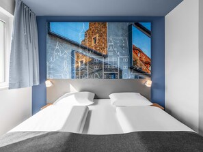 A hotel room with a bed, a window with curtains, and a wall with a cityscape artwork. - B&B Hotel Schweinfurt-City (Schweinfurt)