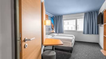 A hotel room with a bed, a desk, a chair, a TV, and a window with curtains.