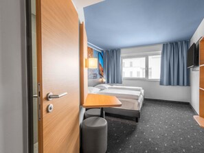 Ein Hotelzimmer mit Bett, Schreibtisch, Stuhl, Fernseher und einem Fenster mit Vorhängen.