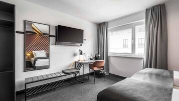 Ein modernes Hotelzimmer mit Bett, Schreibtisch mit Stuhl, Fernseher und großem Fenster mit Vorhängen.