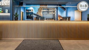 Un espace d’accueil d’hôtel au design moderne, comprenant un comptoir d’accueil, un bar et un escalier menant aux étages supérieurs.