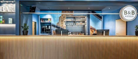 A hotel reception area with a modern design, featuring a reception desk, a bar area, and a staircase leading to upper floors.