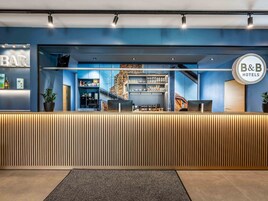 A hotel reception area with a modern design, featuring a reception desk, a bar area, and a staircase leading to upper floors.