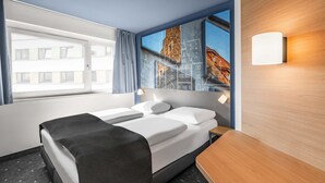 A hotel room with a bed, a nightstand, a window with curtains, and a wall-mounted light. - B&B Hotel Schweinfurt-City (Schweinfurt)