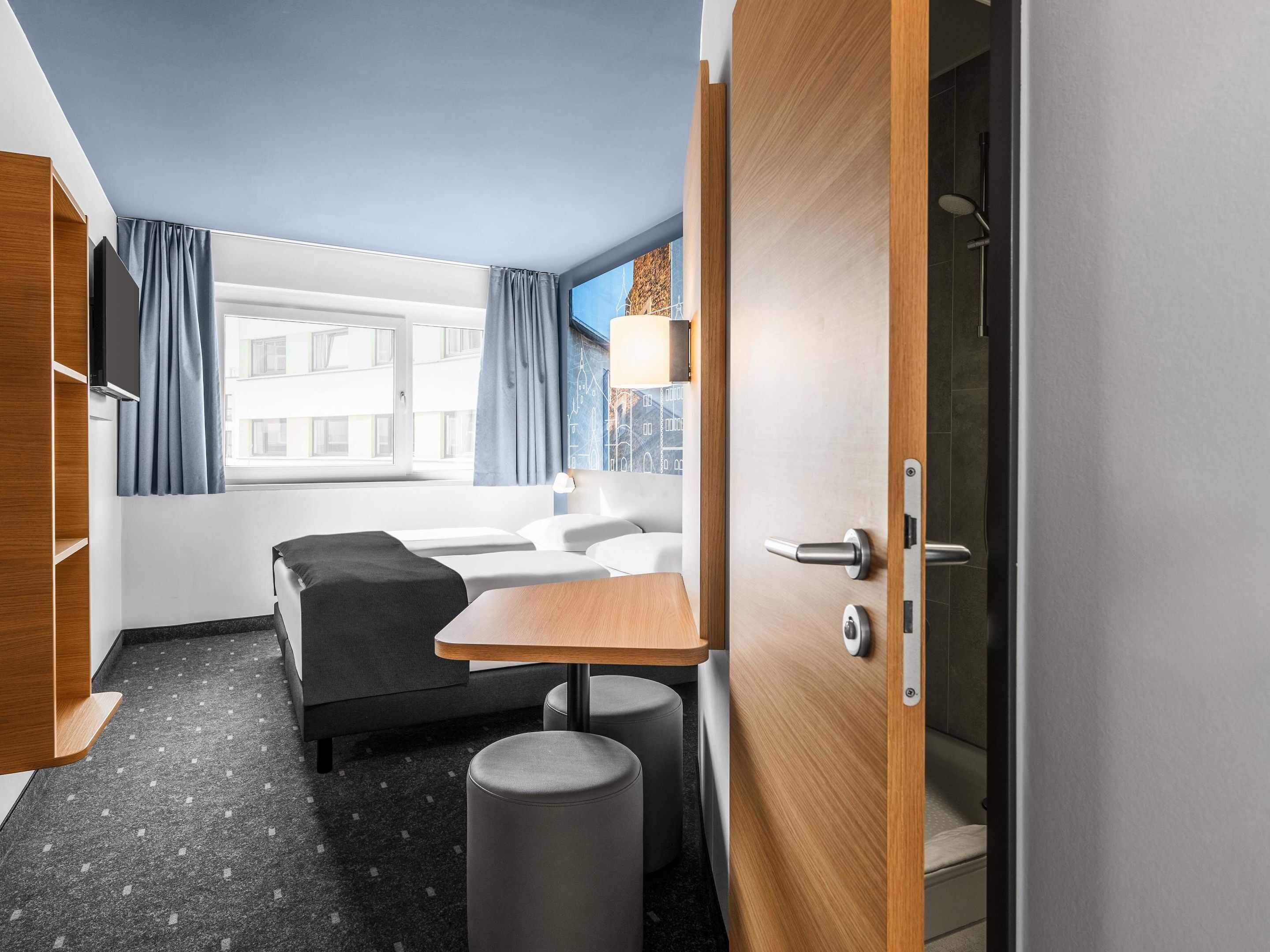 Ein modernes Hotelzimmer mit Bett, kleinem Tisch, Sofa und Duschbereich.