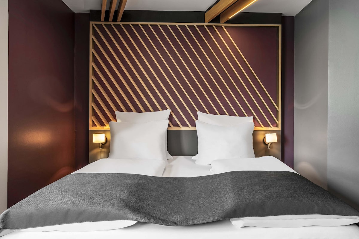Une chambre à coucher moderne avec un lit, deux tables de chevet et une tête de lit à motifs géométriques.