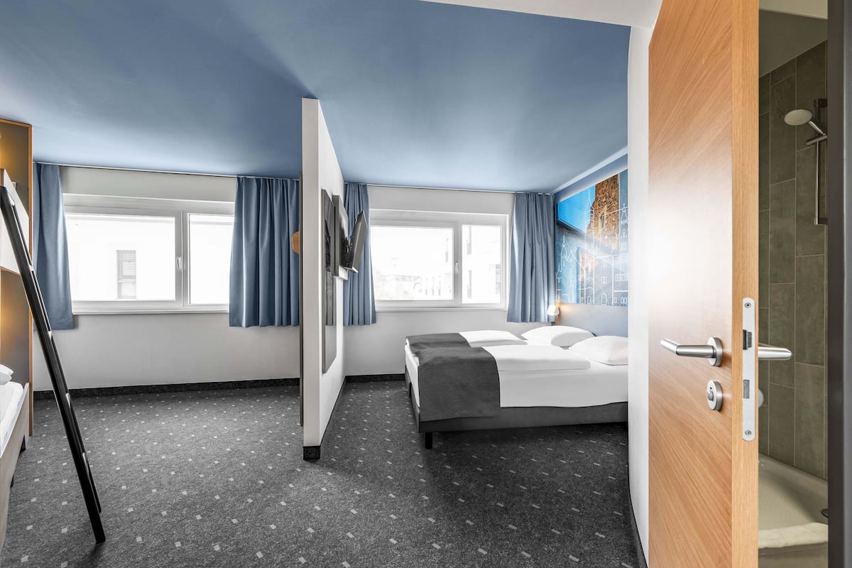 Une chambre d’hôtel comprenant un lit, un bureau, une chaise, une fenêtre avec des rideaux et un espace douche.