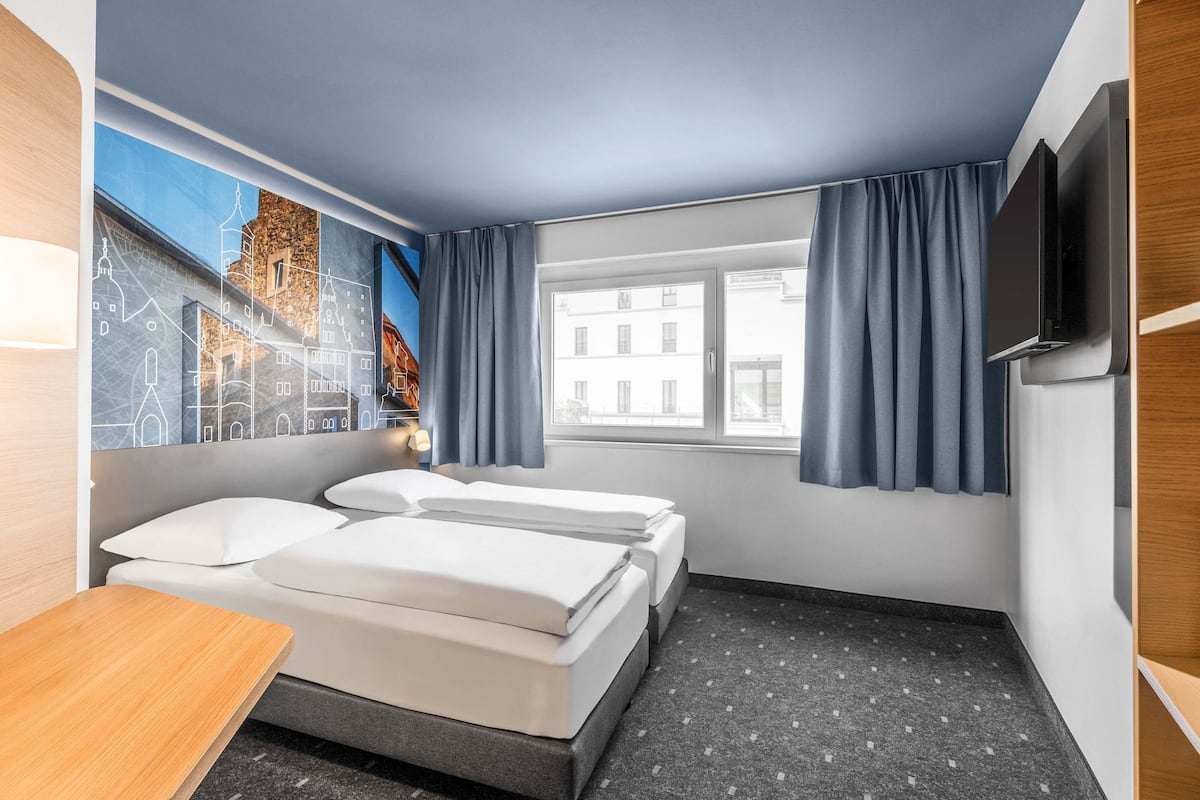 Une chambre d’hôtel avec deux lits, un bureau, une télévision et une fenêtre avec des rideaux.