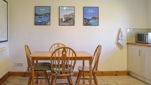 Un coin repas avec une table et des chaises en bois, un coin cuisine équipé d’un four à micro-ondes, et trois tableaux encadrés accrochés au mur.