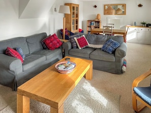 A living room with two grey sofas, a wooden coffee table, a bookshelf, and a dining area with a table and chairs.