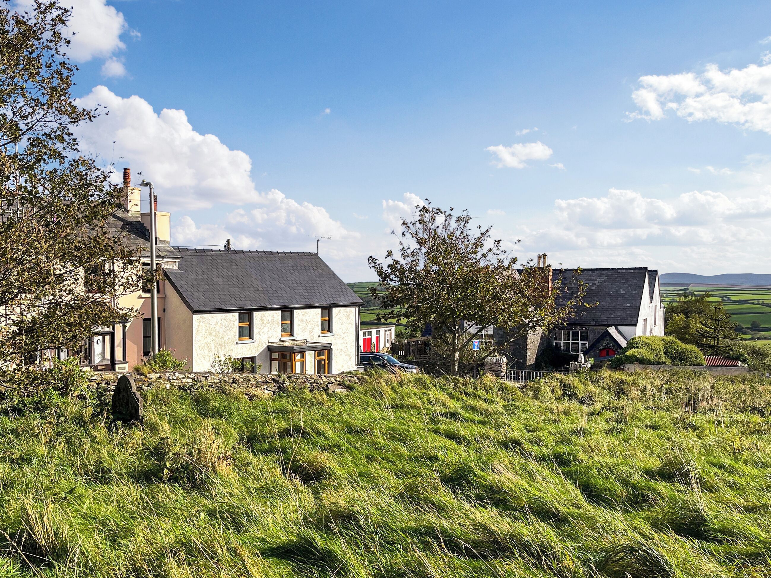 A rural setting with stone houses, a grassy field, and a clear sky.