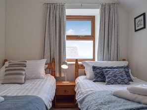 A bedroom with two single beds, a nightstand with a lamp, a window with curtains, and a framed picture on the wall.