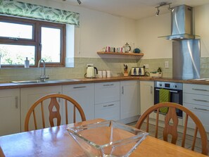 A kitchen with a wooden table, chairs, a window, a shelf with kitchen items, and a stainless steel range hood. - 3 bedroom accommodation in Mathry (Mathry)