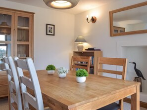 A dining area with a wooden table, white chairs, potted plants, a lamp, and a bookshelf. - 3 bedroom accommodation in Mathry (Mathry)