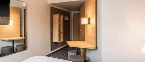 Habitación de hotel con una cama grande, un escritorio, una silla, un espejo y una estantería en la pared.