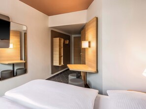 A hotel room with a large bed, a desk, a chair, a mirror, and a wall-mounted shelf. - B&B Hotel Nürnberg-Hbf (Nuremberg)