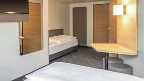 Ett kompakt hotellrum med en säng, ett litet bord, en spegel och en väggmonterad lampa.