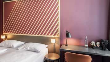 Una camera d'albergo con un letto, due lampade da comodino, una scrivania con una sedia e una bottiglia d'acqua.