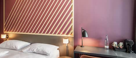 Une chambre d’hôtel comprenant un lit, des lampes de chevet, un bureau avec une chaise et une bouteille d’eau.