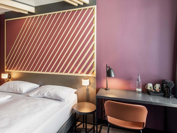A hotel room with a bed, bedside lamps, a desk with a chair, and a water bottle. - B&B Hotel Nürnberg-Hbf (Nuremberg)