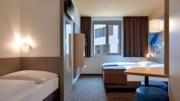 A hotel room with a bed, a desk, a chair, a window with curtains, and a wall-mounted TV.