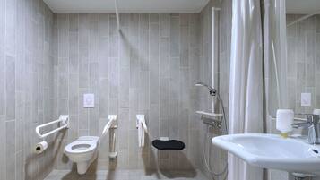 A modern bathroom with grey tiles, a toilet, a bidet, a shower with a handheld showerhead, and a sink with a cup of soap.