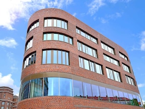 Ein modernes Gebäude mit einer geschwungenen Fassade, großen Fenstern und einem gläsernen, reflektierenden Bereich.