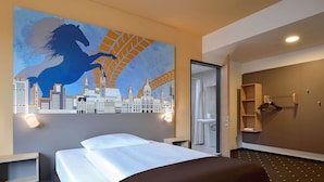 A hotel room with a bed, a cityscape mural, a bathroom with a shower, and a wooden wardrobe. - B&B Hotel Hannover-City (Hannover)
