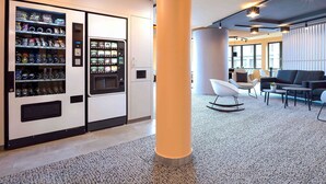 Een moderne lobby met een automaat, zithoek en een grote pilaar.