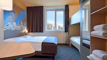 Ein Hotelzimmer mit zwei Betten, einem Schreibtisch, einem Stuhl, einem Fenster mit Vorhängen, einem Wandbild und einer Ablage mit Handtüchern.
