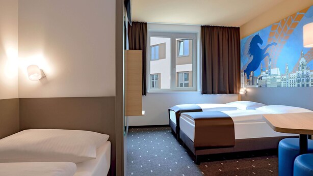 Een hotelkamer met twee bedden, een stadslandschap muurschildering, een raam met gordijnen en een kamerkleed met dessin.