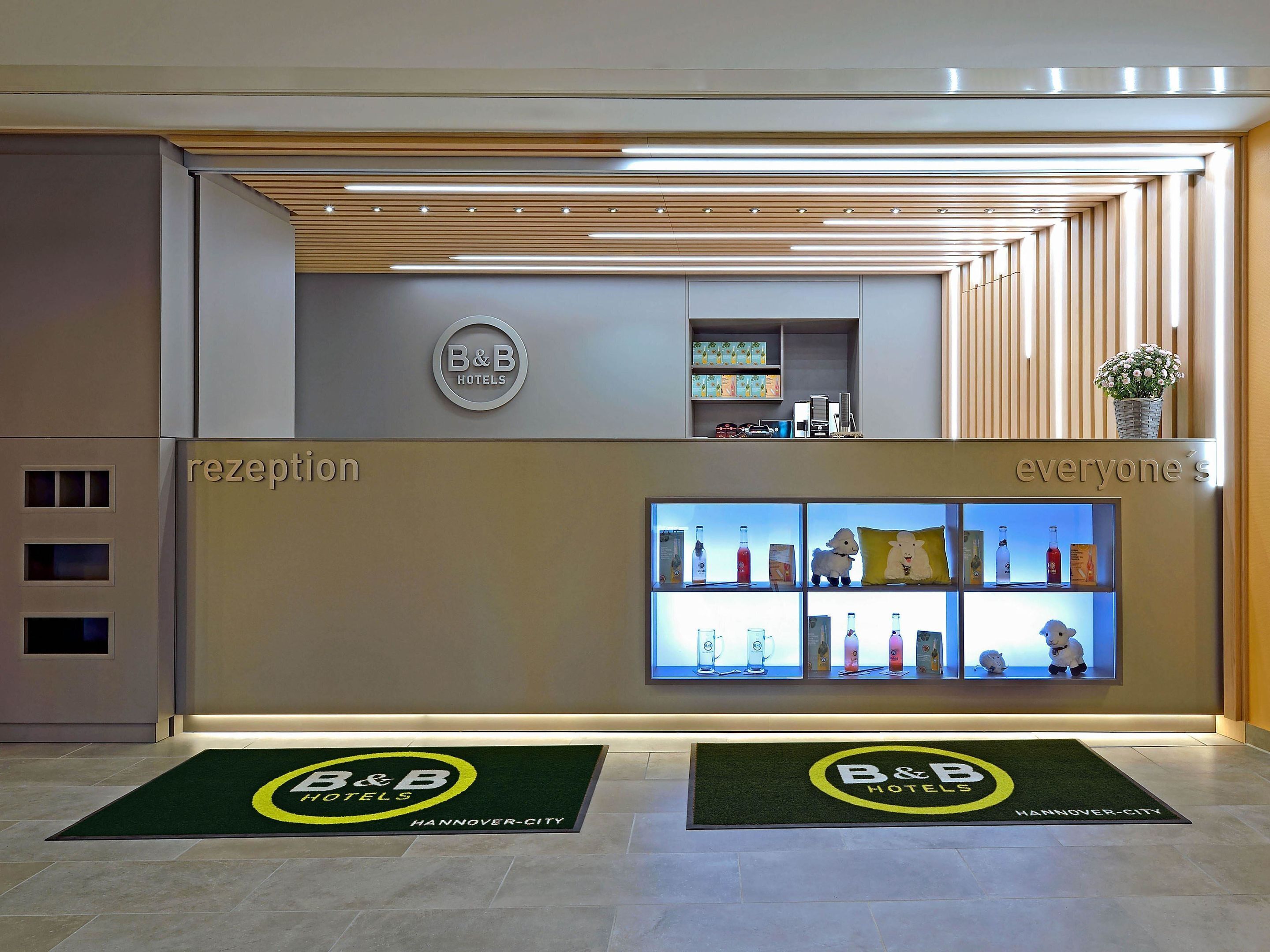 A B&B hotel reception area with a modern design, including a reception desk, a display of amenities, and a welcome mat.