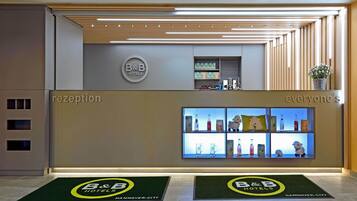 A B&B hotel reception area with a modern design, including a reception desk, a display of amenities, and a welcome mat.