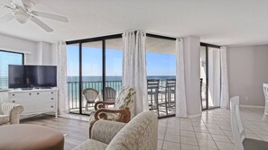 Un salón amplio con un televisor grande, asientos cómodos y un balcón con vistas al mar.