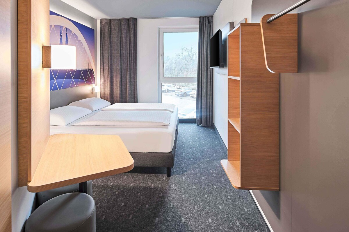 Habitación de hotel moderna con cama, escritorio, silla, televisor y vista al exterior.