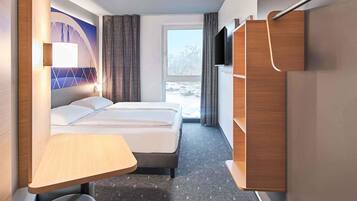 A modern hotel room with a bed, a desk, a chair, a TV, and a view of the outside.