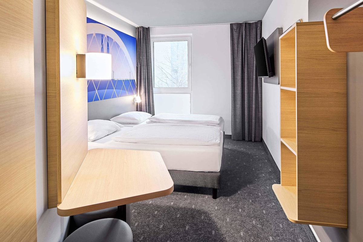 A hotel room with a bed, a desk, a wardrobe, and a window with curtains.