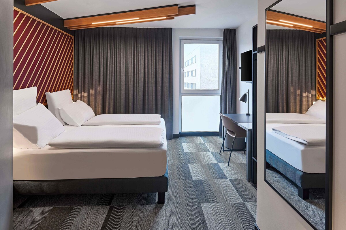 Habitación de hotel moderna con dos camas, un escritorio y un ventanal grande.