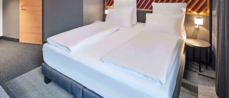 A modern hotel room with a neatly made bed, a wooden door, and a unique geometric wall design.
