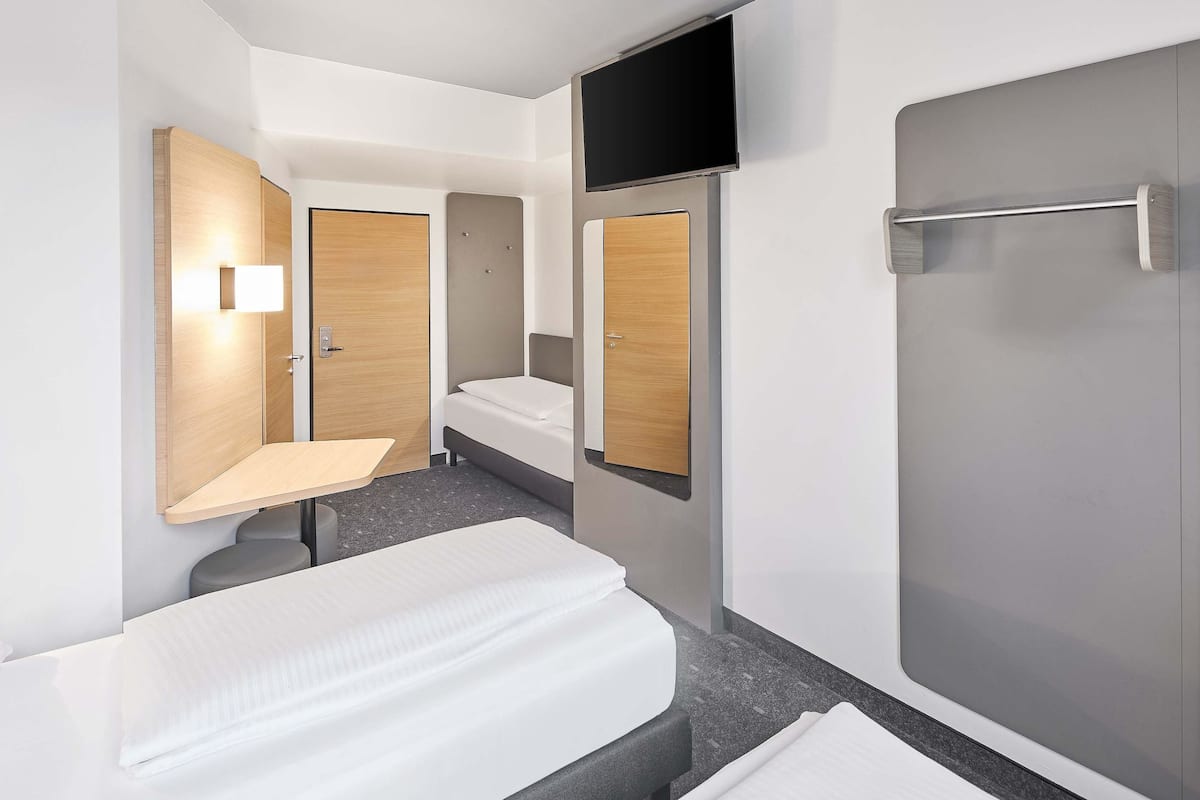 A modern hotel room with a bed, a small desk, a mirror, a TV, and a shower area.