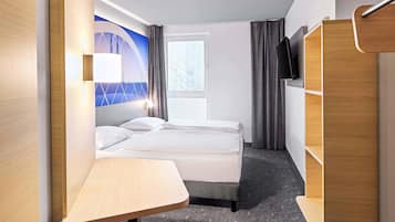 A hotel room with a bed, a desk, a wardrobe, and a window with curtains.