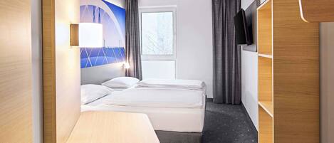 A hotel room with a bed, a desk, a wardrobe, and a window with curtains.