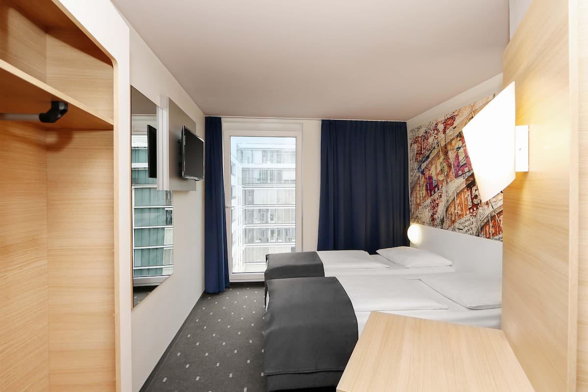 Habitación de hotel con cama, mesita de noche, televisor y ventana con cortinas.
