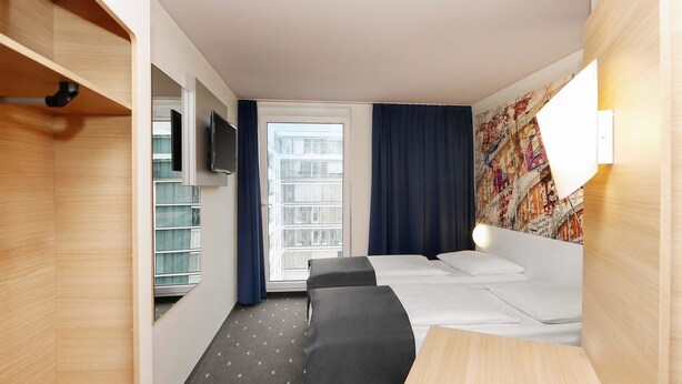 A hotel room with a bed, bedside table, TV, and a window with curtains. - B&B Hotel Berlin-Alexanderplatz (Berlin)
