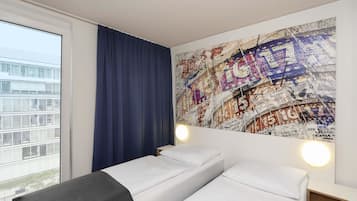 Ein Hotelzimmer mit großem Fenster, einem Bett mit weißen Leinentüchern, einem blauen Vorhang und Wandkunst mit einer Weltkarte.