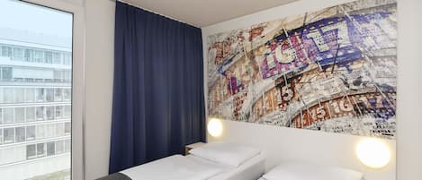 Une chambre d’hôtel avec une grande fenêtre, un lit recouvert de draps blancs, un rideau bleu et un mur orné d’une carte du monde.